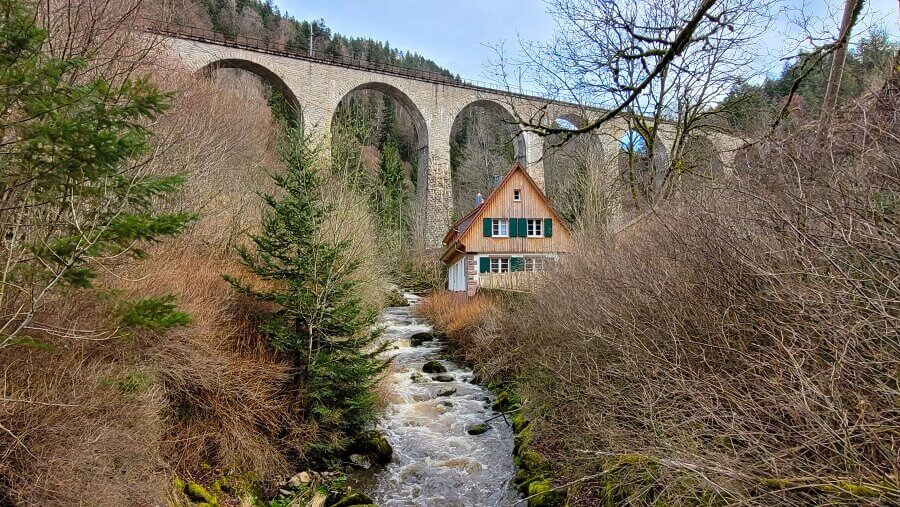 Malerisches Haus an einem Fluss unterhalb einer Bahnbrücke