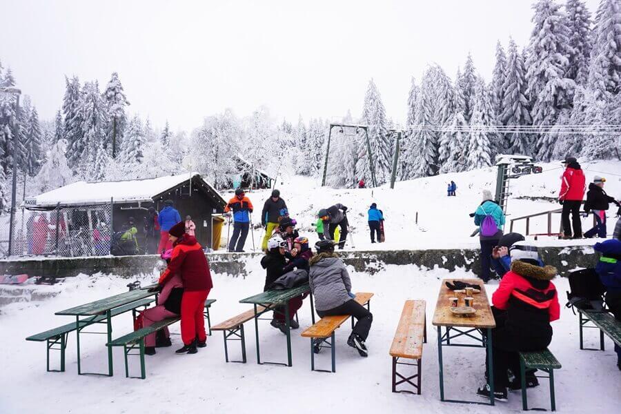 Wintersportler sitzen an einem Skihang an Biertischen