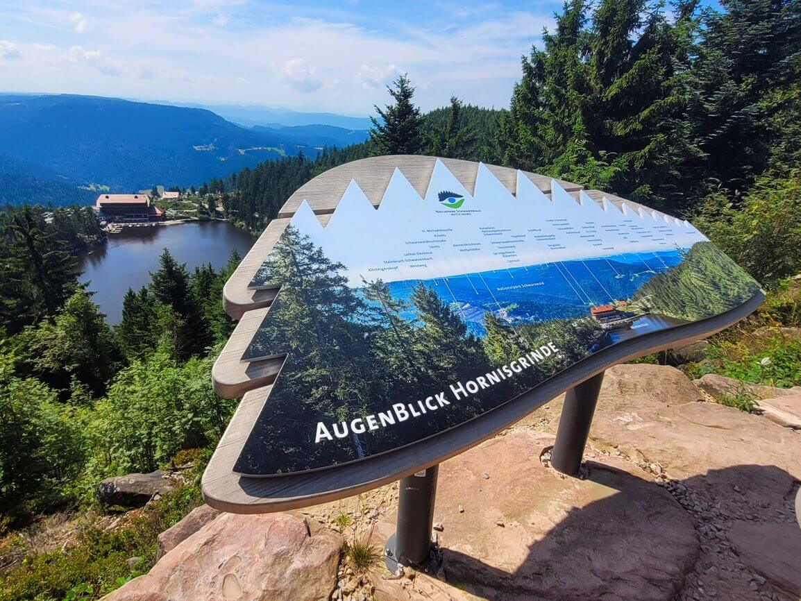 Informationstafel zu einem Wanderweg oberhalb eines Bergsees