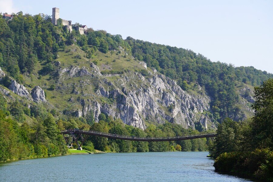 Das Wahrzeichen des Altmühltals: die Holzbrücke Tatzlwurm! Brücke über einen Fluss und eine Burg im Hintergrund
